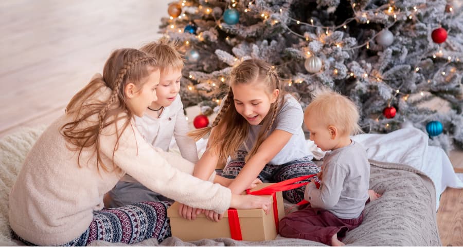 Kids opening a gift in the family room near a Christmas tree.